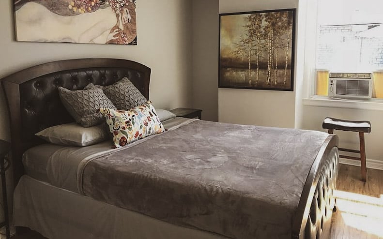 photo of a bed made with grey bedding and artwork on the walls