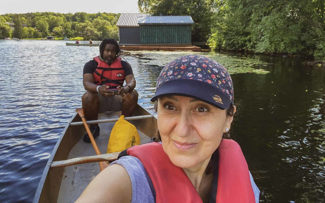 A woman taking a selfie in a canoe on a lake with a man in the canoe behind her