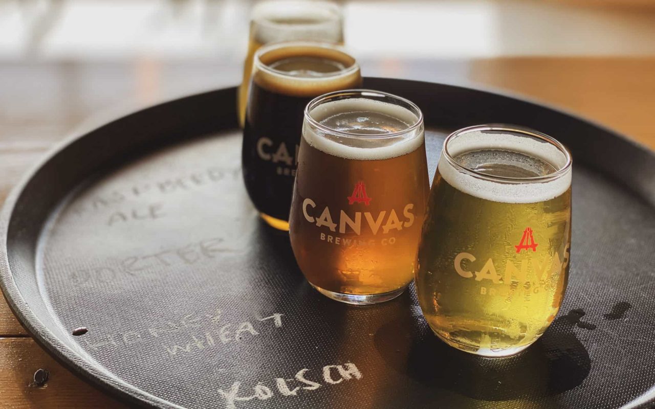 a flight of beer on a tray in Canvas Brewing Co glasses