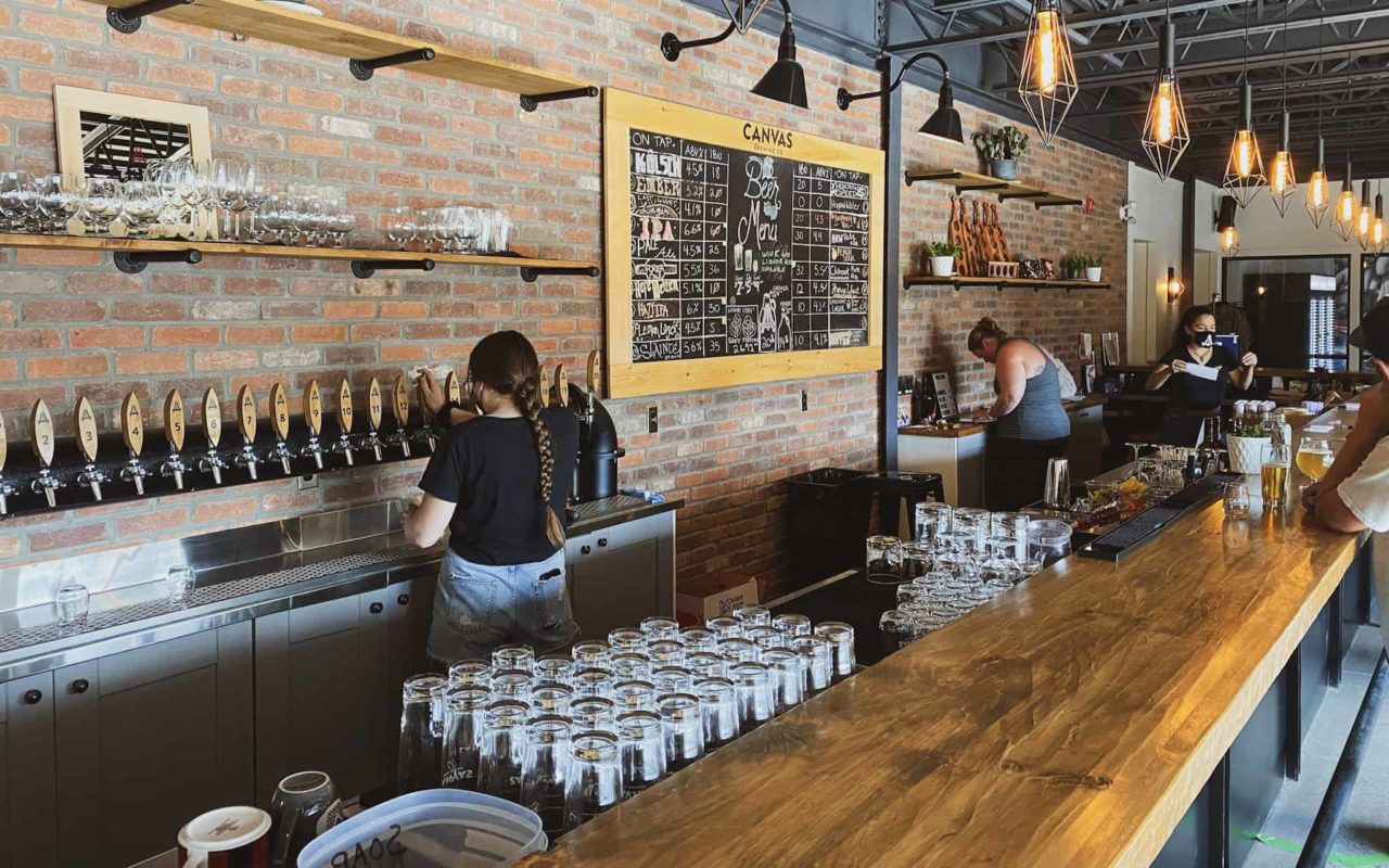 a view of the bar inside Canvas Brewing Co. with three women tending bar