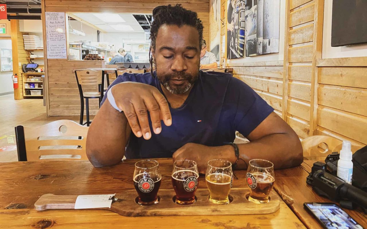 a man seated at a table looking at a flight of 4 beers on the table in front of him