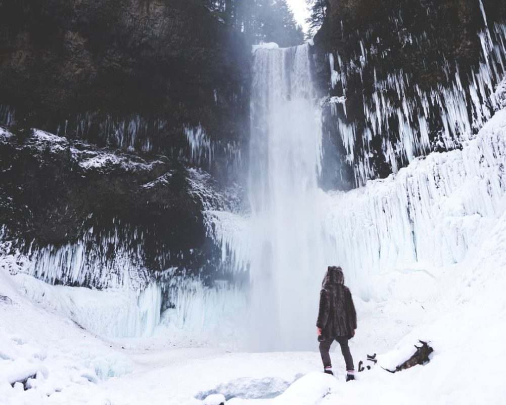 person standing at the base of a waterfall surrounded by snow in winter | ontario winter activities