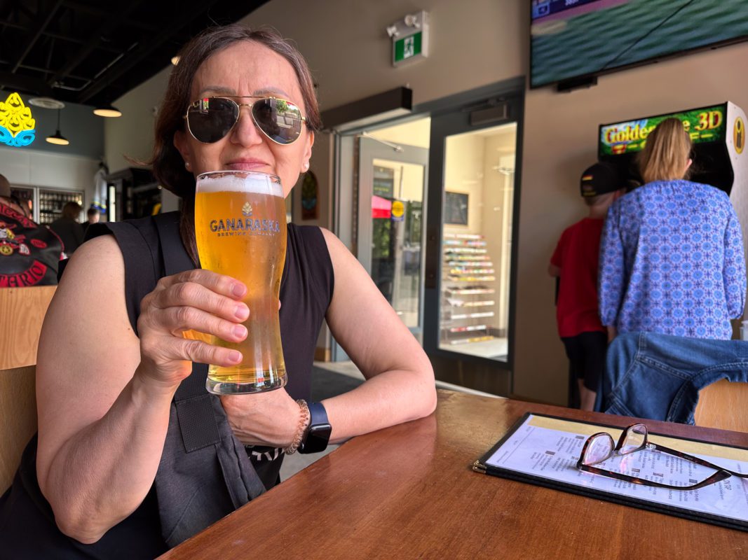 A woman holding up a pint of beer while seated in Ganaraska Brewing Company, Port Hope