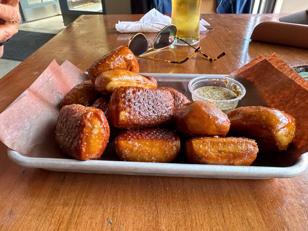 a plate of pretzel bites with a dipping sauce in the center of a wooden table