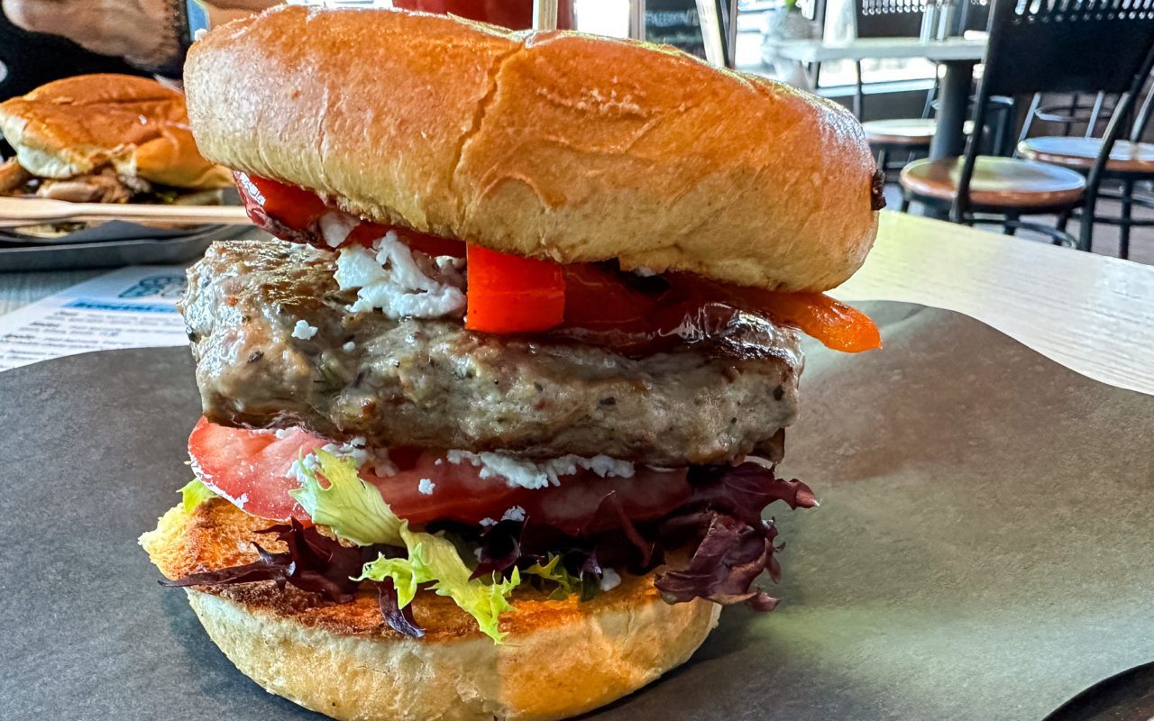a close-up view of a loaded hamburger with lettuce, tomatoes, and red peppers
