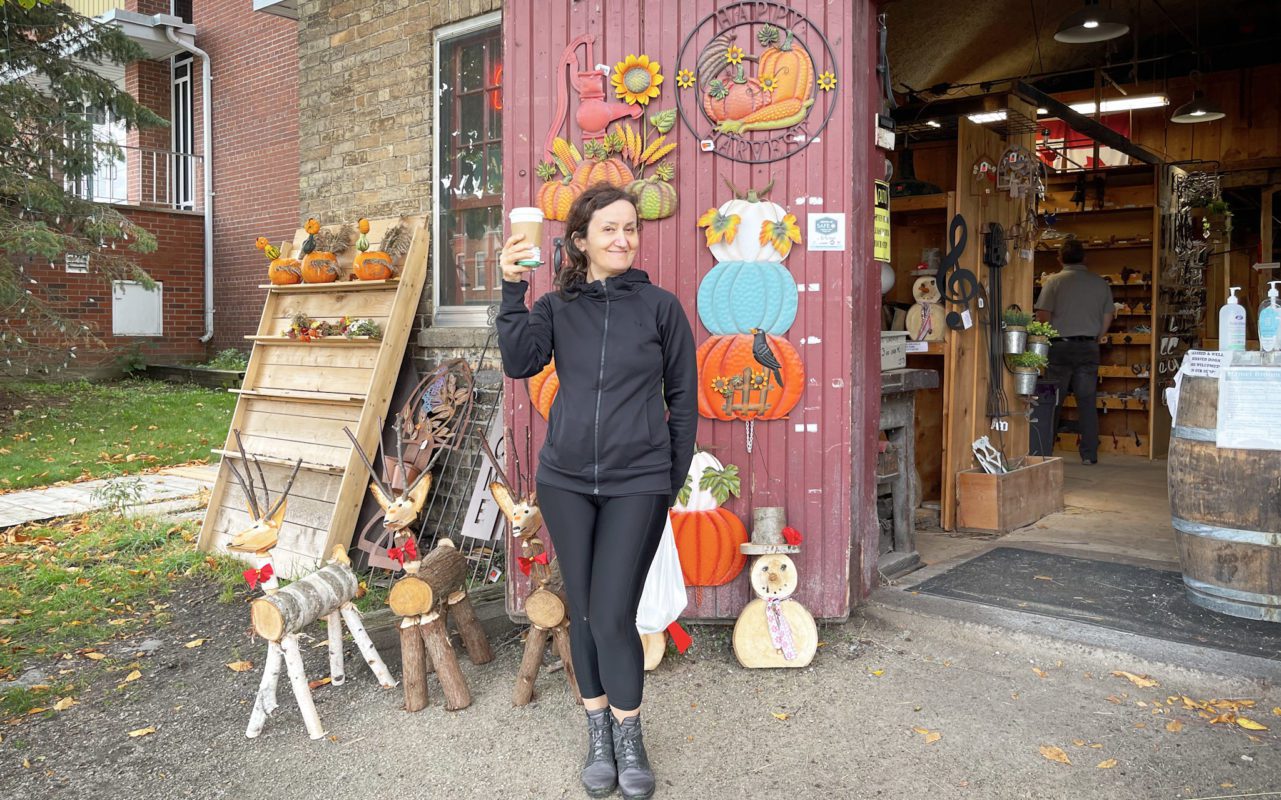A woman holding up a cup of coffee in front of a small shop | st jacobs tourism