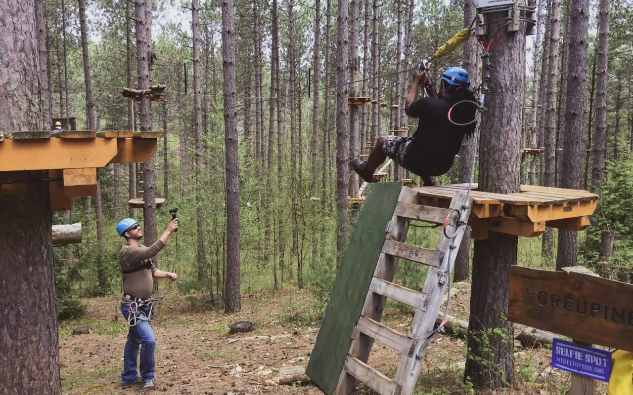 a person getting ready to zipline while another person watches from the ground at treetop eco-adventure park