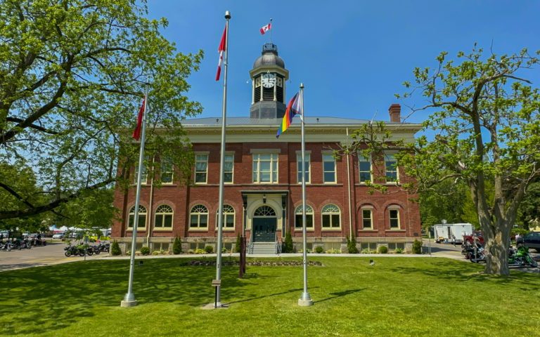 large brick building with many windows and flag poles on the front lawn in Port Hope, Ontario
