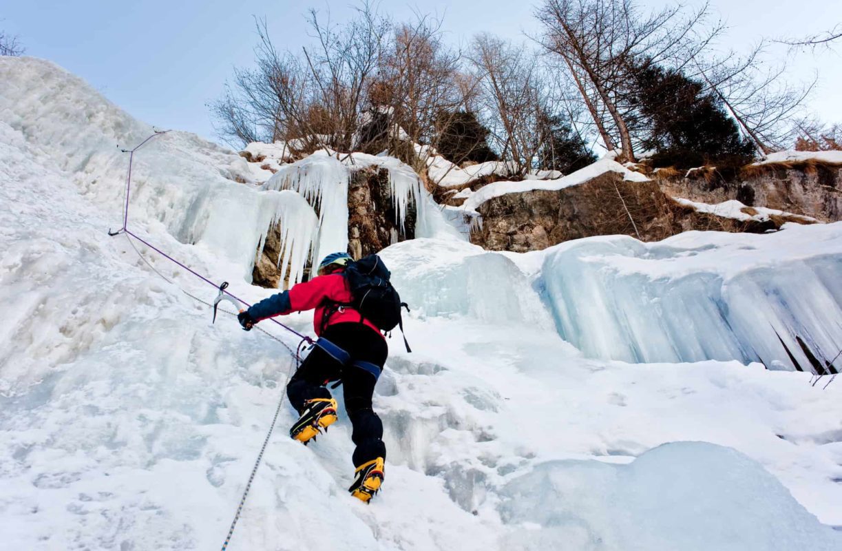 a person climbing an icy cliff with full climbing gear | things to do in winter ontario