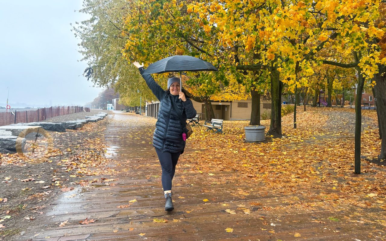a woman holding an umbrella and walking on a wet path with yellow leaves - toronto lakefront