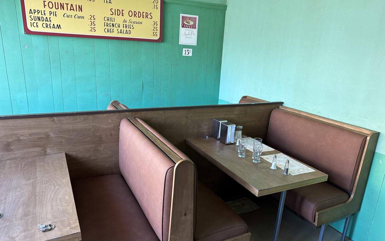 Old dining booth, set with glasses, placemats, salt, and pepper, with a menu on the wall