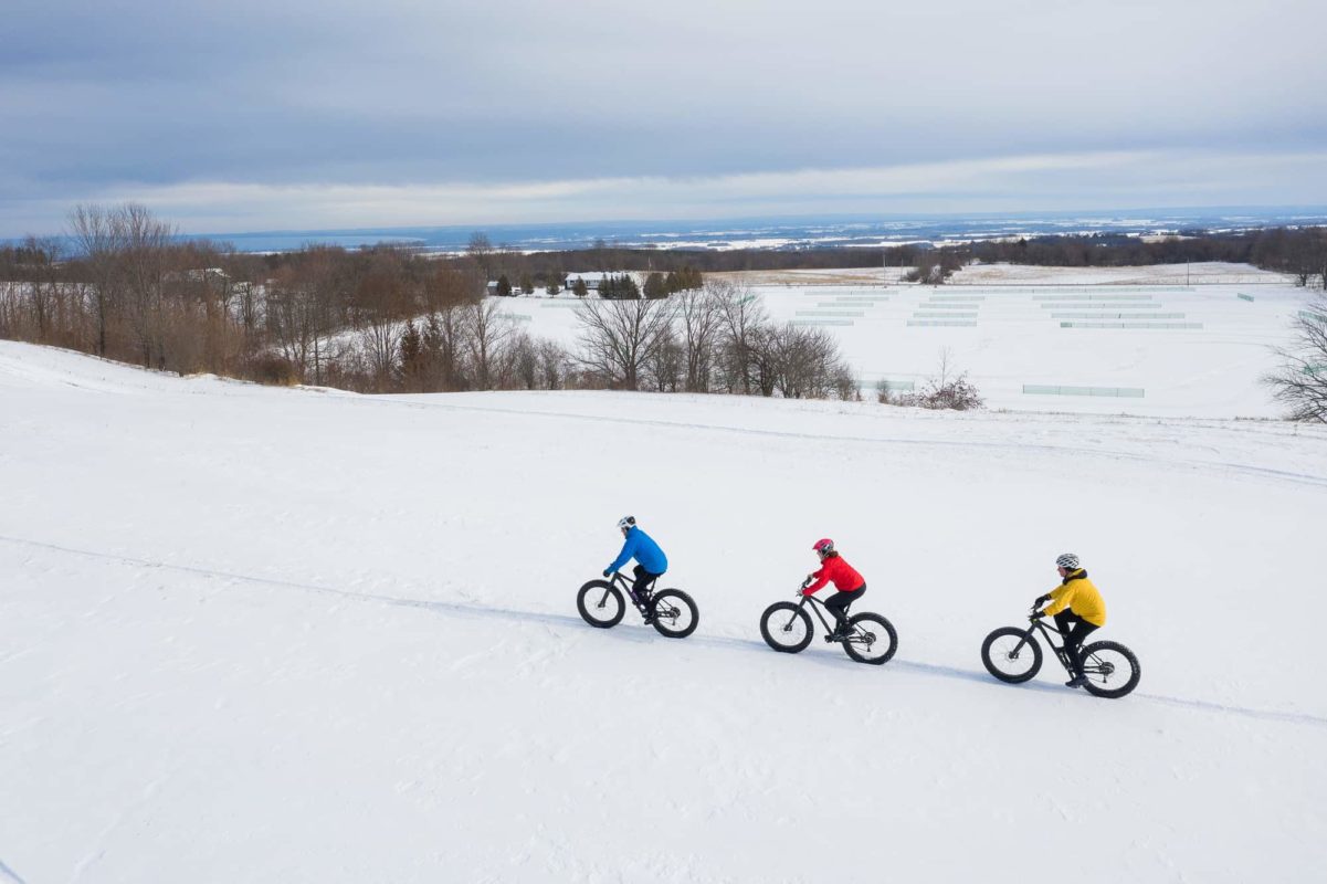 three people fat biking through a snow covered field | winter activities ontario