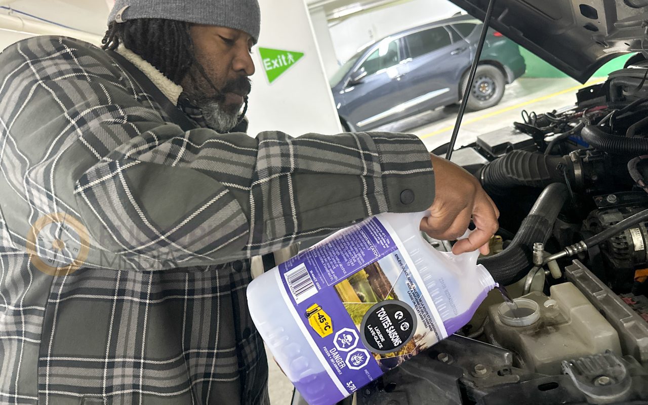 a man pouring a liquid into a car engine - winter driving safety